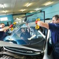 Automobile glaziers workers replacing windscreen or windshield of a car in auto service station garage